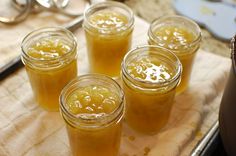 four jars filled with yellow liquid sitting on top of a wooden cutting board next to scissors