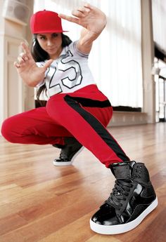 a woman in black and white shirt and red pants doing a dance pose on the floor