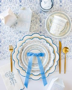 a table setting with blue and white plates, napkins, and gold utensils