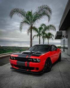 a red and black dodge car parked in front of a building next to palm trees