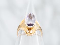 This sophisticated ring is crafted from yellow gold and features a unique Art Nouveau-style design. A large amethyst cabochon is set into the center of the ring, adding a stunning splash of color. This piece of jewelry is truly a once-in-a-lifetime find!Metal: 14K Yellow GoldGem: Amethyst 3.50 CaratsGem Measurements: 7.5 x 15.5 mm, OvalRing Size: 6.25Marks: "A*14K" Stamped on the inside band Modern Yellow Gold Amethyst Gemstone Ring, Modern Gold Amethyst Gemstone Ring, Modern Yellow Gold Amethyst Ring, Modern Gold Oval Amethyst Ring, Modern Gold Amethyst Ring With Oval Shape, Gold Amethyst Oval Cabochon Ring, Modern Gold Amethyst Ring, Yellow Gold Amethyst Cabochon Ring, Gold Amethyst Ring With Cabochon Cut