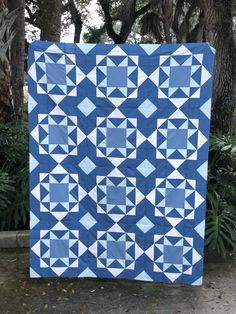 a blue and white quilt is on display in front of some trees at the park