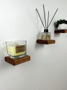 three wooden shelves holding candles, soaps and other items on white wall behind them