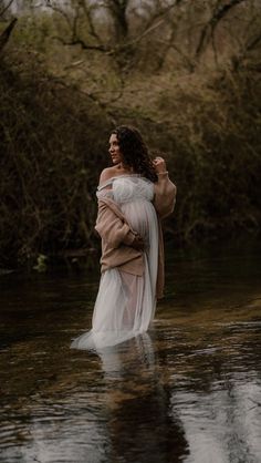 a woman is standing in the water wearing a white dress and holding her arms around her waist