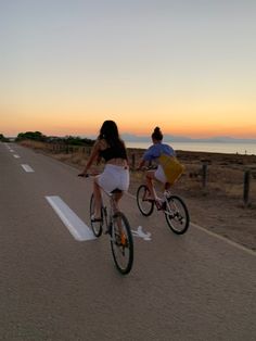 two people riding bikes down the road at sunset