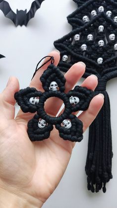 a hand holding a black beaded brooch with skulls on it and a bat in the background