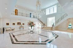 a large foyer with marble floors and chandelier in the center is flanked by two grand staircases