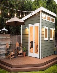 a small backyard shed with patio furniture and lights hanging from the roof over it's deck