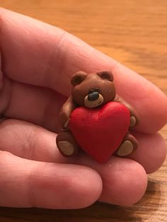 a small teddy bear holding a red heart in its hand on a wooden table top