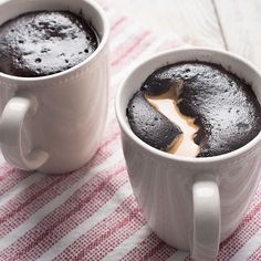 two white mugs filled with chocolate cake on top of a red and white table cloth