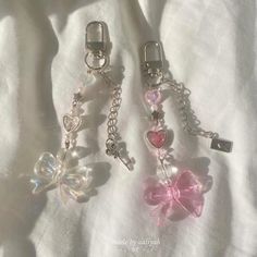 three charms with bows and hearts attached to them on a white sheet, one has a key chain