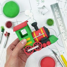 a hand holding a toy train on top of a table next to other craft supplies