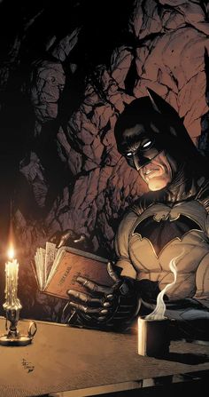 a batman sitting at a table reading a book with a candle in front of him