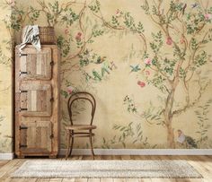 a chair sitting next to a wooden cabinet in front of a wall with flowers and birds on it