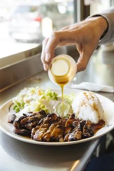 a person pouring dressing over a plate of food