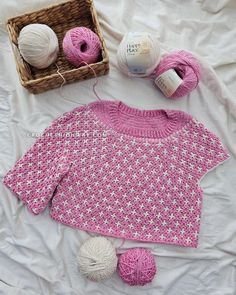 a knitted sweater and balls of yarn on a bed with a basket of knitting needles