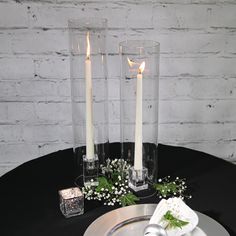 two candles are sitting on a table with napkins and flowers in glass vases