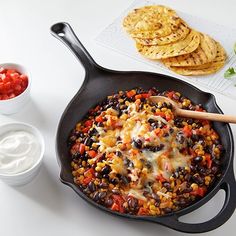 a skillet filled with black beans, cheese and tortilla chips next to some sour cream