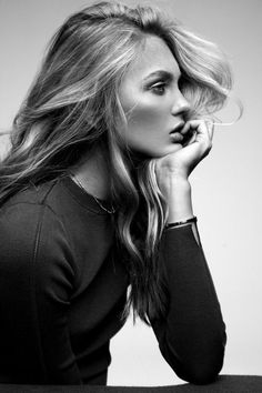 a woman with long blonde hair posing for a black and white photo, her hand on her face