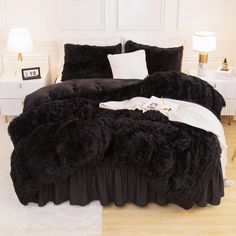 a bed with black comforter and pillows in a white room next to a lamp