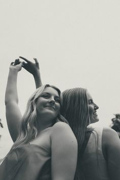 two women standing next to each other with their arms in the air and one holding her hand up