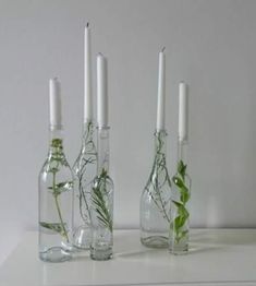 three glass bottles with plants in them on a white shelf next to candles and flowers