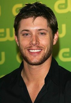 a close up of a person wearing a black shirt and smiling at the camera with a green background