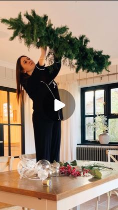 a woman is holding up a christmas tree over her head while standing on a table