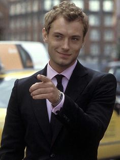 a man in a suit pointing to the left with his hand on his hip and wearing a watch