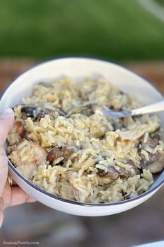 a person is holding a bowl of rice with mushrooms and meat in it while outside