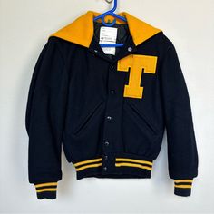 This Is A Vintage Letterman / Varsity Jacket For Women And It’s In Great Vintage Condition. Navy Blue Wool Blend With Yellow Accent Colors. “T” Is The Letter On The Jacket. It Was Found In Texas, But I Don’t Know What School This Is From. The Name Katherine Hudson Is Embroidered On The Inside. Quilted Interior. Hood On The Back That Is Mostly Worn As A Sailor Type Collar. The Hood Can Zip Up Into A Hood, But It’s Difficult As The Zipper Is Quite “Sticky.” Rib Knit At The Wrist And Bottom. Snaps Collegiate Winter Outerwear For School, Collegiate Outerwear For School In Fall, Collegiate Outerwear With Pockets For Fall, Collegiate Navy Outerwear For Fall, Collegiate Style Navy Outerwear For Fall, Fitted Yellow Hooded Outerwear, Yellow Varsity Winter Outerwear, Yellow Varsity Outerwear For Winter, Casual Yellow Outerwear For College