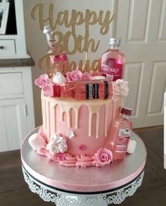 a birthday cake decorated with pink and white icing, flowers, and liquor bottles