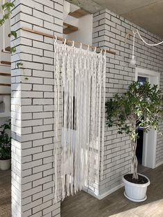 a white brick house with a potted tree in the corner and curtains hanging from the ceiling