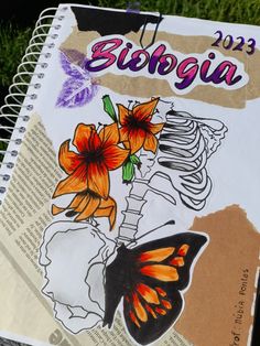 a spiral notebook with an image of a butterfly and flowers on the cover, sitting in grass