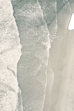 an aerial view of the ocean with waves coming in to shore and people walking on the beach