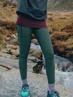 a woman standing on top of a rock next to a river wearing green leggings