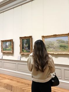 a woman looking at paintings on display in a museum