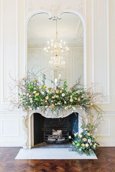 an ornate fireplace with flowers and greenery in front of a mirror on the wall