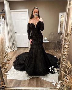 a woman taking a selfie in front of a mirror wearing a long black dress