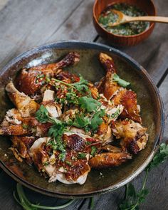 a plate full of chicken and garnishes on a wooden table next to a bowl of sauce