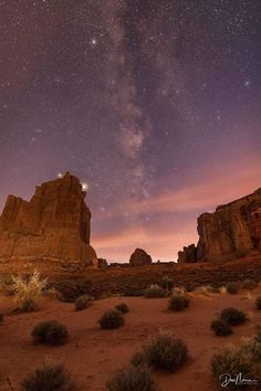 the night sky is filled with stars above some rocks and bushes in the desert area