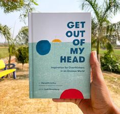 a hand holding up a book in front of a park with benches and palm trees