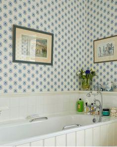 a bath tub sitting next to a wall with pictures on the wall and flowers in a vase