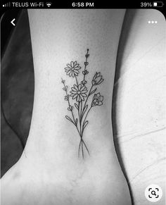 a small flower tattoo on the ankle with daisies and leaves in black ink,