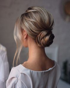 a woman with blonde hair styled into a low bun in a white blouse, looking off to the side