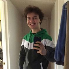 a young man is taking a selfie in the mirror with his cell phone while wearing a green and white hoodie