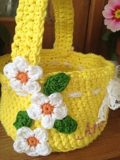 a crocheted yellow basket with flowers on the handle and handles is sitting on a table