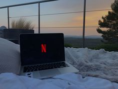 a laptop computer sitting on top of a bed next to a white comforter and pillows