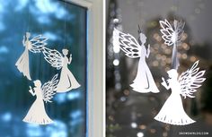 paper cut angels hanging from a window next to a christmas ornament in front of a window