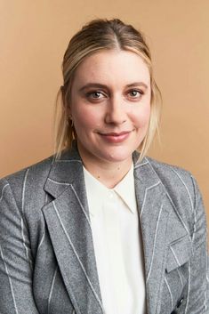 a woman with blonde hair wearing a gray jacket and white shirt smiles at the camera